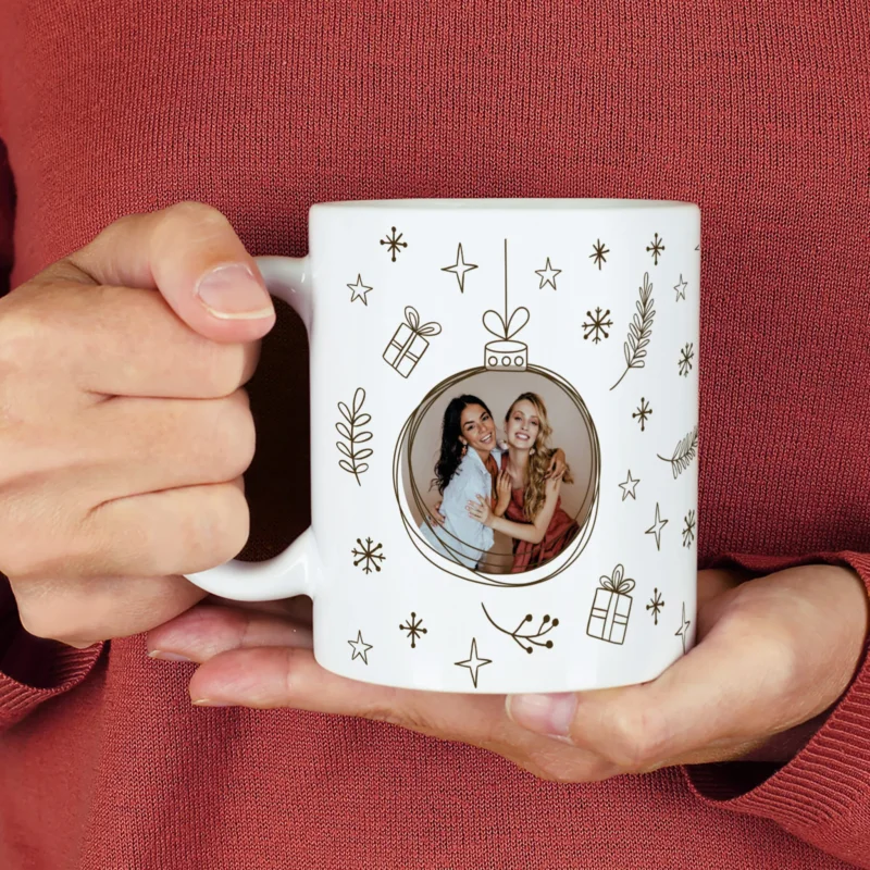 Weiße Fototasse mit Weihnachtskugel-Design in Schwarz und integriertem Foto – festlich mit Sternen und Geschenken dekoriert.