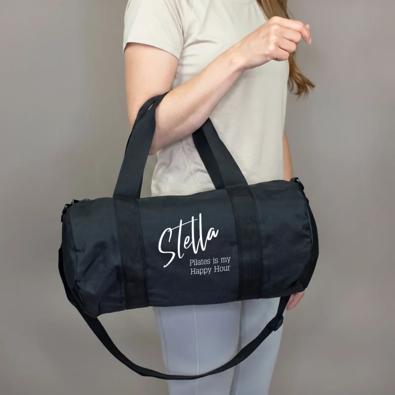 Schwarze personalisierte Sporttasche mit Name Stella und Wunschtext Pilates is my Happy Hour, getragen von einer Frau