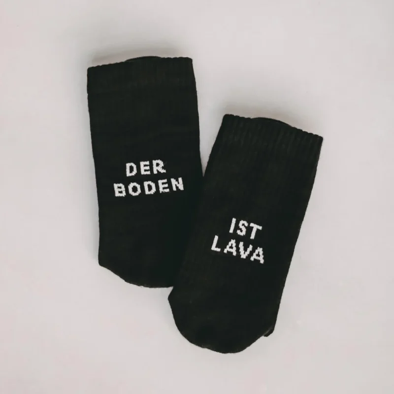 Schwarze Socken mit Schriftzug „DER BODEN“ und „IST LAVA“